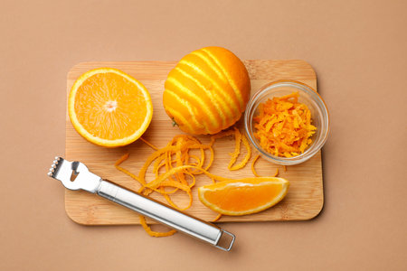 Orange zest, fresh fruits and zester tool on beige background, top view