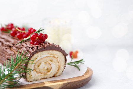 Delicious Yule log (traditional Christmas cake) with redcurrant and fir tree branches on light table, closeup. Space for textの写真素材