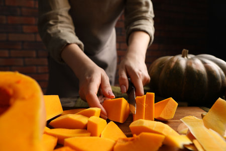 Woman cutting pumpkin at table against brick wall, closeupの写真素材