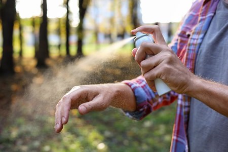 Man spraying tick repellent onto arm in park, closeup. Space for textの写真素材