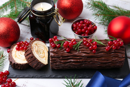 Delicious Yule log (traditional Christmas cake) with redcurrant, decor and fir tree branches on light wooden table, closeupの写真素材