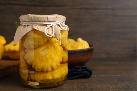 Pickled pattypan squashes in glass jar on wooden table, closeup. Space for textの写真素材