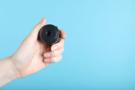 Woman with hidden camera on light blue background, closeup. Space for text