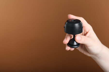 Woman with hidden camera on brown background, closeup. Space for text