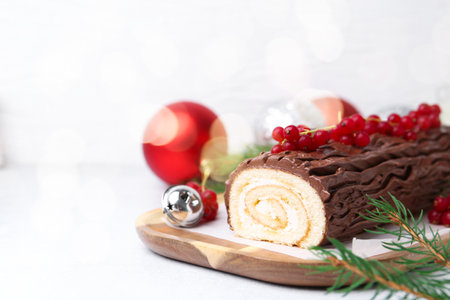 Delicious Yule log (traditional Christmas cake) with redcurrant, decor and fir tree branches on light table, closeup. Space for textの写真素材