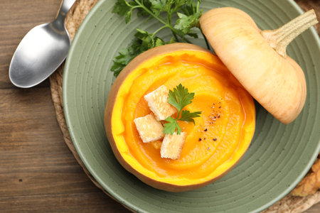 Tasty pumpkin cream soup with parsley and croutons served in pumpkin on wooden table, top viewの写真素材