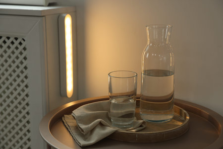 Table with water and portable LED lamp on wall at home