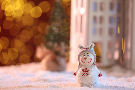 Cute decorative snowman on artificial snow against blurred lights. Space for textの写真素材