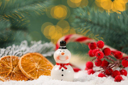 Cute decorative snowman, branch with red berries and dried orange slices on artificial snow against blurred background, closeupの写真素材