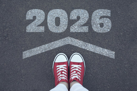 Woman standing in front arrow and numbers 2026 on asphalt, top viewの写真素材