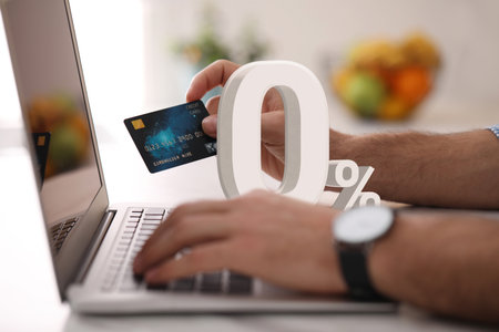 Man with credit card using laptop at table, closeup. 0 percent sign above computer. Zero commissionの写真素材