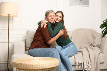 Mother and daughter hugging on sofa at homeの写真素材