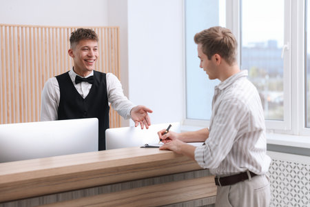 Receptionist working with guest at reception desk in hotelの写真素材