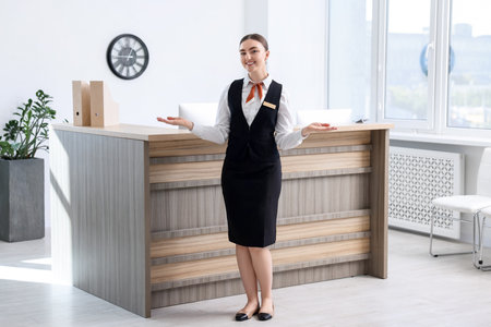Happy receptionist welcoming near reception desk indoorsの写真素材