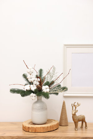 Beautiful composition with fir tree branches in vase and reindeer figure on wooden table near white wall indoors.の写真素材