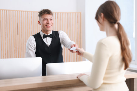 Receptionist giving hotel key card to guest at reception desk indoors, selective focusの写真素材