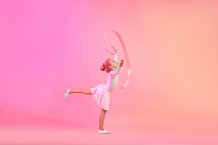 Cute little girl with ribbon doing gymnastic exercise on pink gradient backgroundの写真素材
