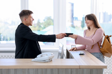 Receptionist giving passport to guest at reception desk indoorsの写真素材