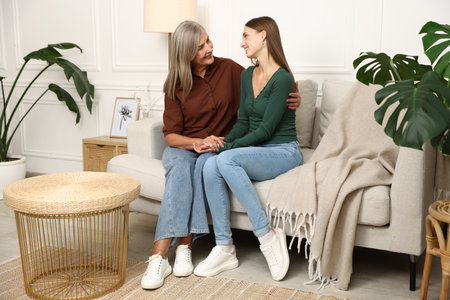 Mother and daughter hugging on sofa at homeの写真素材