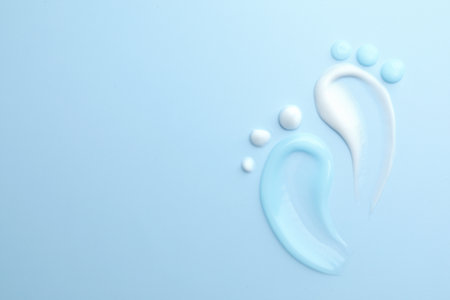 Feet shape made of samples of different cosmetic products on light blue background, flat lay. Space for textの写真素材