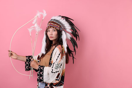 Shaman woman in native American Indian headdress with bow and arrows on pink background.
