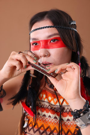 Shaman woman playing harmonica on pale brown backgroundの写真素材