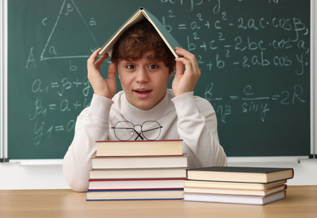 Back to school. Student with books and stationery at wooden desk against chalkboard with math assignment indoorsの写真素材