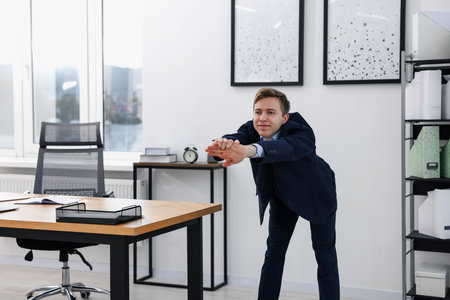 Young businessman doing stretching exercise in officeの写真素材