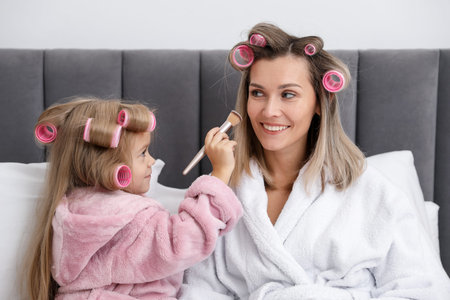Little girl doing her mom's makeup on bed at homeの写真素材