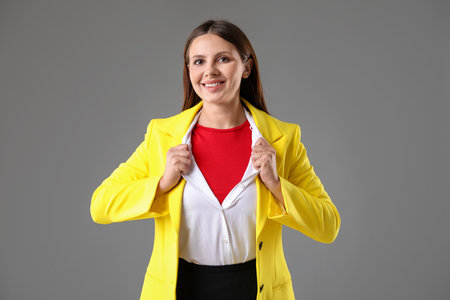Businesswoman wearing superhero costume under her clothes on gray backgroundの写真素材