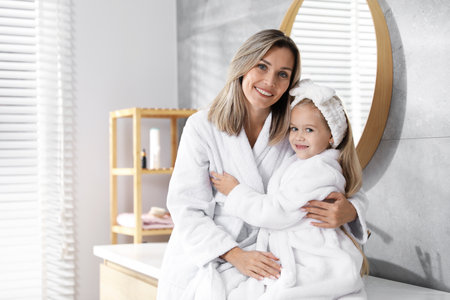 Happy mother and daughter in bathrobes at bathroom. Space for textの写真素材