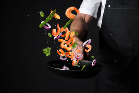 Chef tossing ingredients in pan against black background, closeupの写真素材