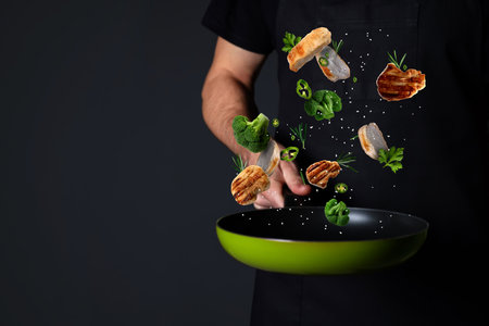 Chef tossing ingredients in pan against black background, closeupの写真素材