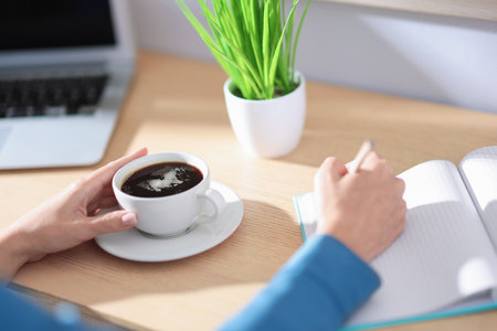 Woman with notebook and pencil having coffee break at wooden table indoors, closeupの写真素材