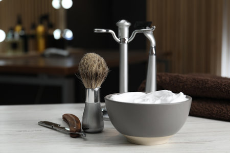 Shaving brush, razors and bowl of foam on light wooden table in barbershop, closeupの写真素材