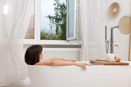 Woman taking bath in bathroom with open windowの写真素材