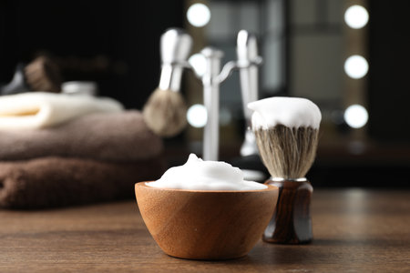 Shaving brush and foam on wooden table in barbershop, closeupの写真素材