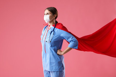 Medical worker wearing protective mask and superhero cape on pink backgroundの写真素材