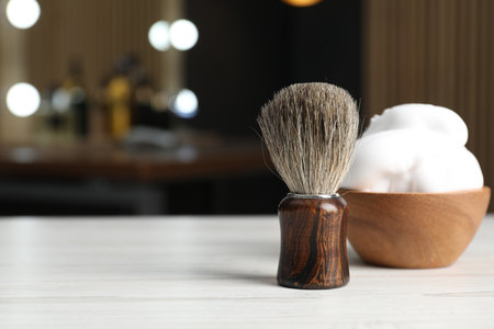 Shaving brush and bowl of foam on light wooden table in barbershop, closeup. Space for textの写真素材