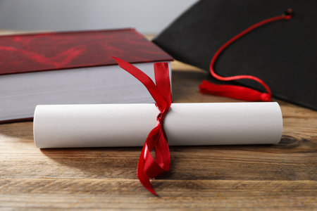 Graduation cap, book and diploma on wooden table, closeupの写真素材