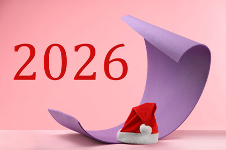 Happy New Year 2026 greeting card with Santa Claus hat and yoga mat on pink backgroundの写真素材