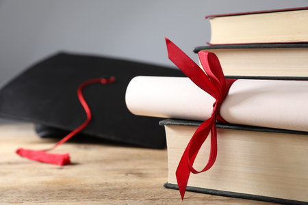 Graduation cap, diploma and books on wooden table, selective focusの写真素材