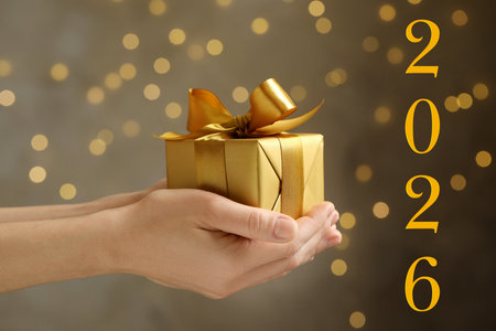 Happy New Year 2026 greeting card. Woman holding gift box against blurred lights, bokeh effectの写真素材