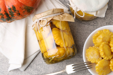 Pickled pattypan squashes in jars, bowl and fork on gray textured table, flat layの写真素材