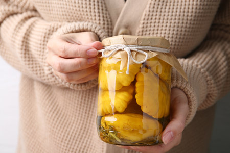 Woman with glass jar of pickled pattypan squashes against light background, closeupの写真素材