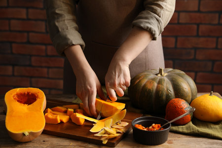Woman cutting pumpkin at wooden table against brick wall, closeupの写真素材