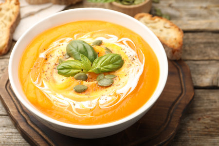 Delicious pumpkin cream soup with basil and seeds served on wooden table, closeupの写真素材