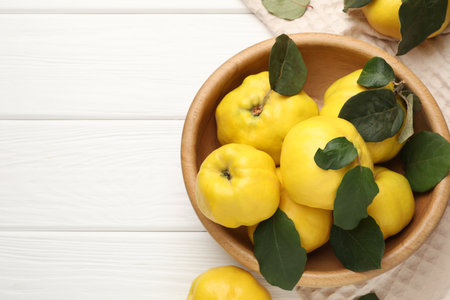 Fresh ripe quinces with leaves on white wooden table, flat lay. Space for textの写真素材