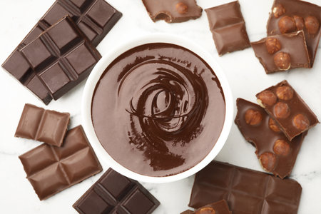 Bowl with melted chocolate and pieces on white table, flat layの写真素材