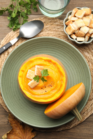Tasty pumpkin cream soup with parsley and croutons served in pumpkin on wooden table, flat layの写真素材